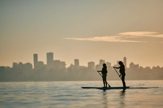 Two people are seen in silhouette paddleboarding in Vancouver